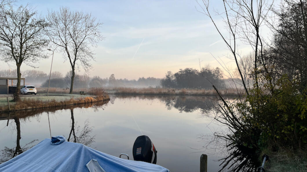 uitzicht op de ringvaart en het Twiske. Met blauw zeil bedekte boot op de voorgrond