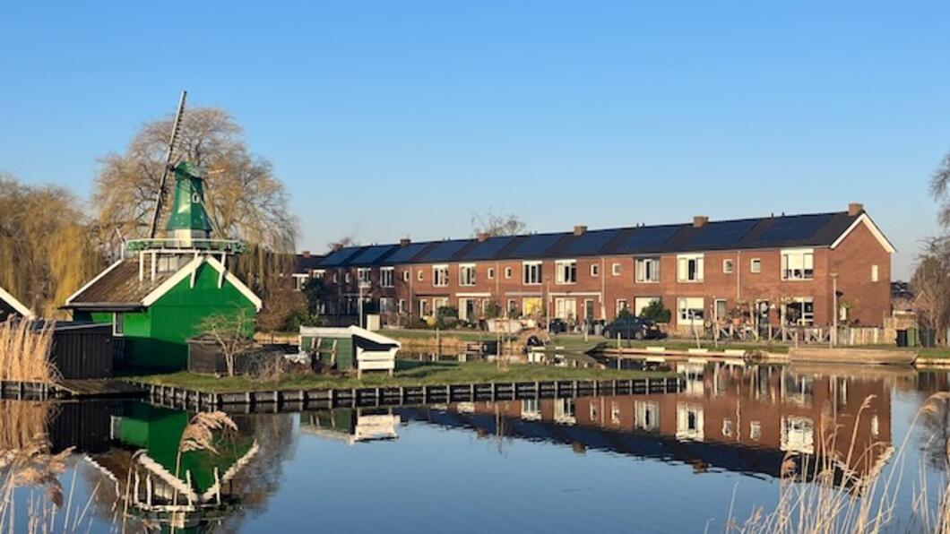 Foto van een kleine groene molen en sociale huurhuizen met zonnepanelen op het dak